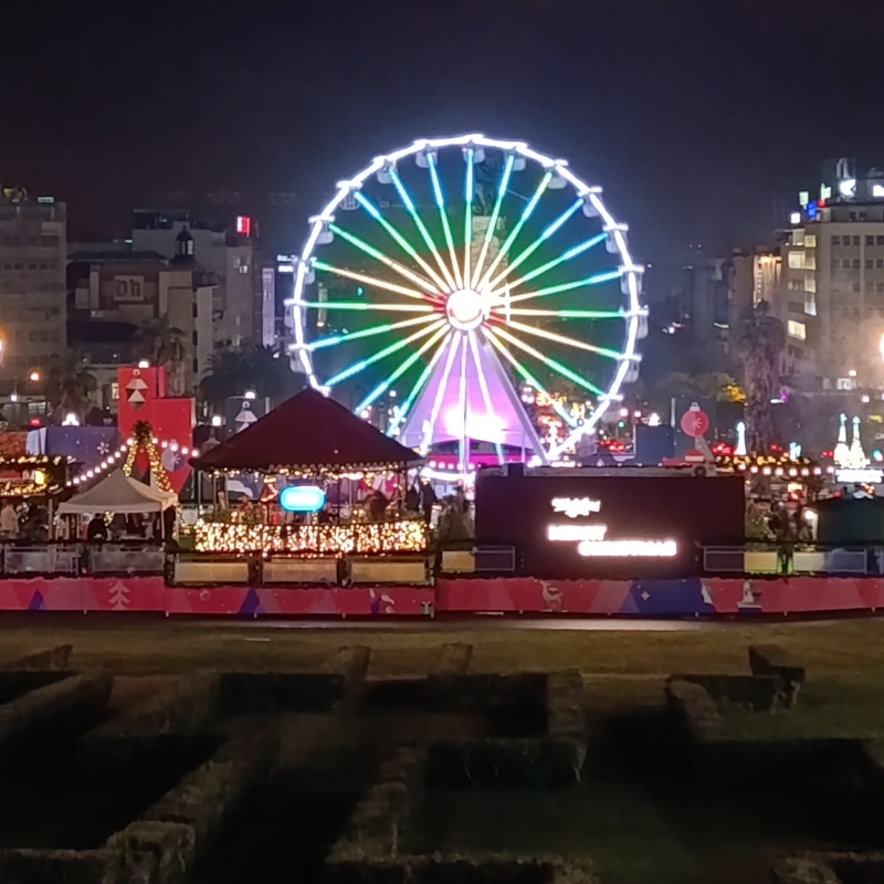 Illuminated Ferris wheel at Wonderland Lisboa 2025 Christmas market at night with city buildings in the background