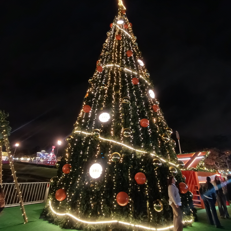 Massive, brightly decorated Christmas tree with golden and red ornaments and string lights at Wonderland Lisboa 2025.