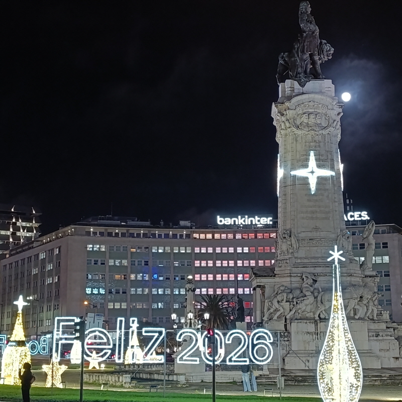 Night view of Praça dos Restauradores in Lisbon with a monument and neon lights wishing